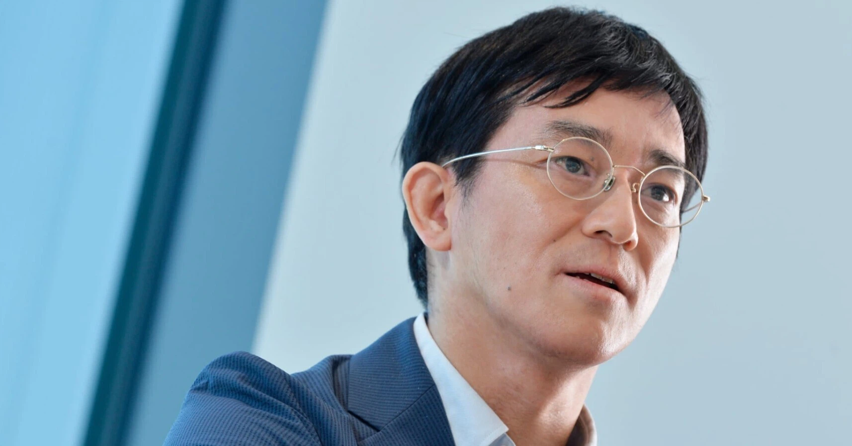 青い背景の前で話す合同会社ポスト石油戦略研究所代表の大場紀章さん